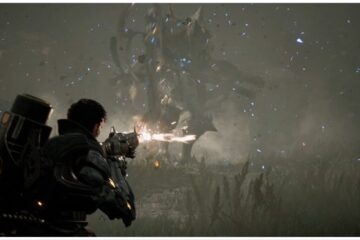 feature image for our the first descendant tier list, the image features a promo screenshot of a character holding a gun while firing it towards a large monster ahead, they are walking across grass and weeds as speckles of dust and debris fly through the air